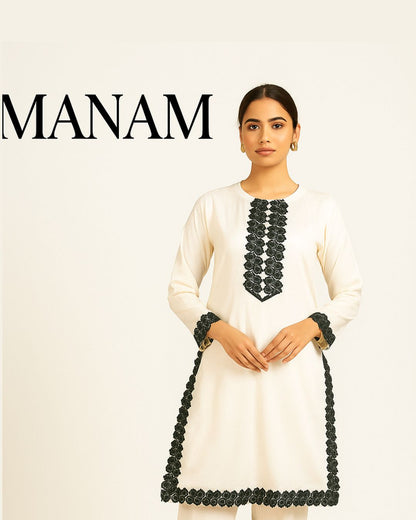 Woman wearing a white dress with black  lace embroidery, with 'MANAM' branding above.